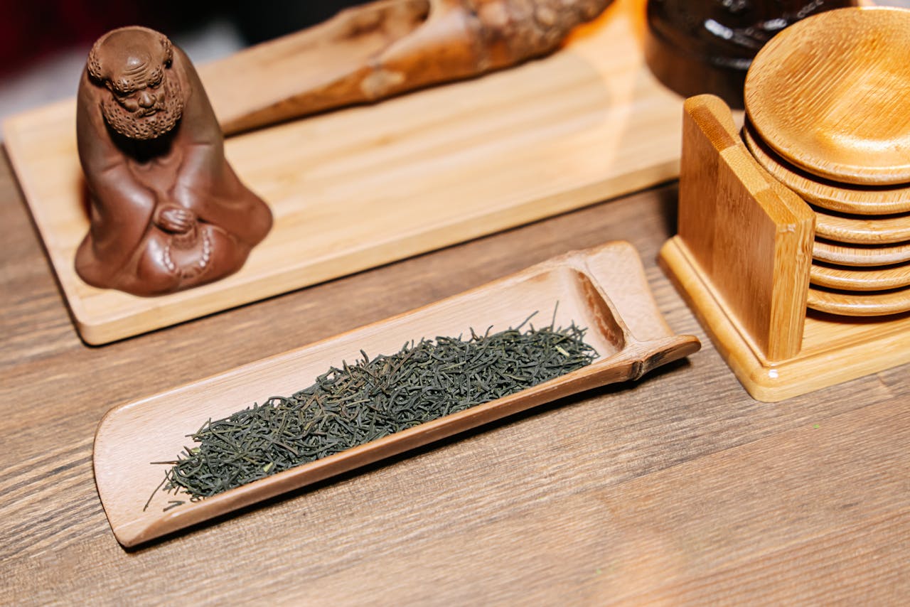 Green tea leaves showcased on wooden tray with traditional tea ceremony setup.
