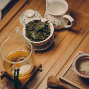 Warm, inviting tea ceremony scene with traditional teapot, leaves, and cup on a wooden table.